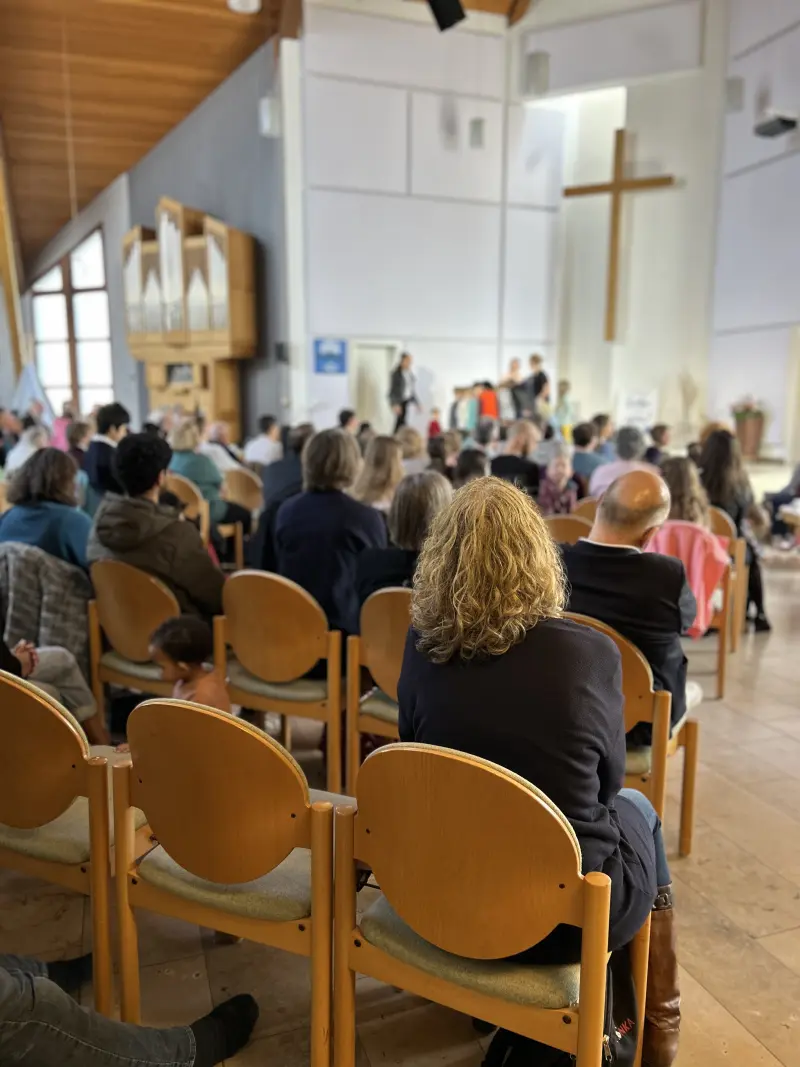 Blick von hinten auf eine sitzende Menschenmenge während eines Gottesdienstes oder einer Veranstaltung in einer Kirche.
