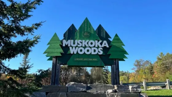 Ein Schild mit der Aufschrift „Muskoka Woods – A resort just for kids“ vor einem klaren blauen Himmel.