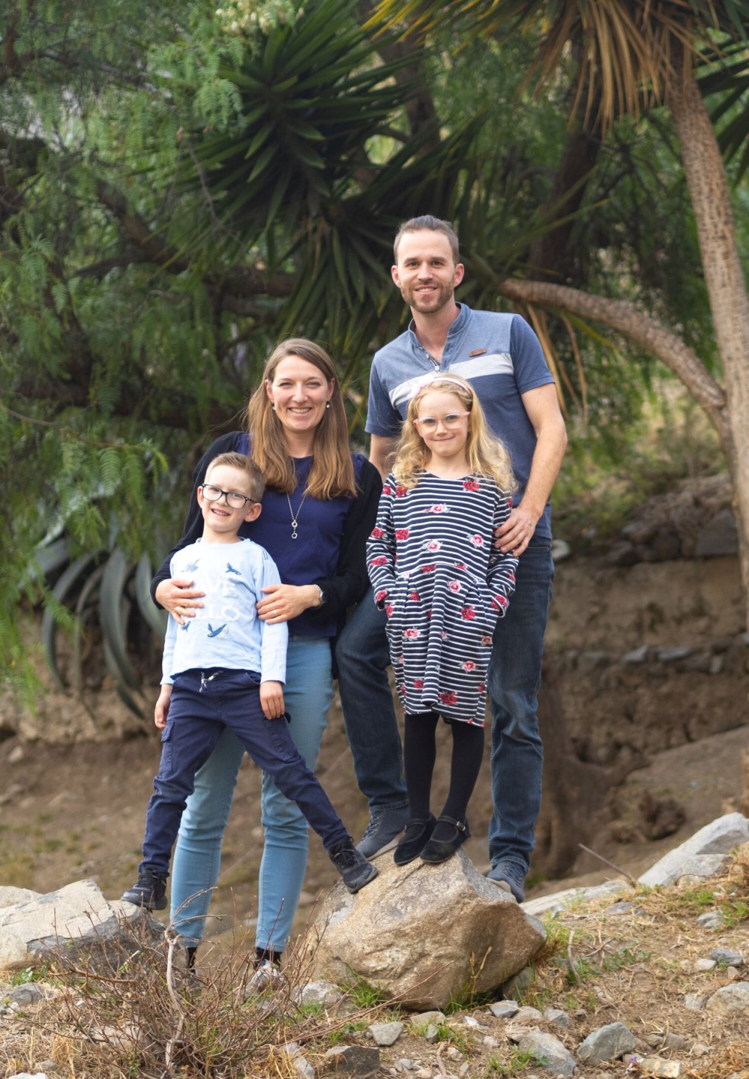 Eine vierköpfige Familie lächelt in einer Gartenlandschaft in die Kamera.